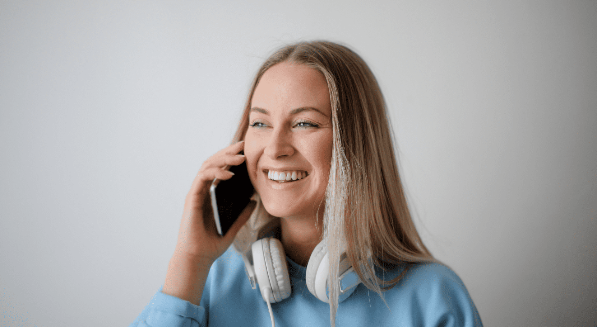 Woman smiling, talking on phone with headphones.